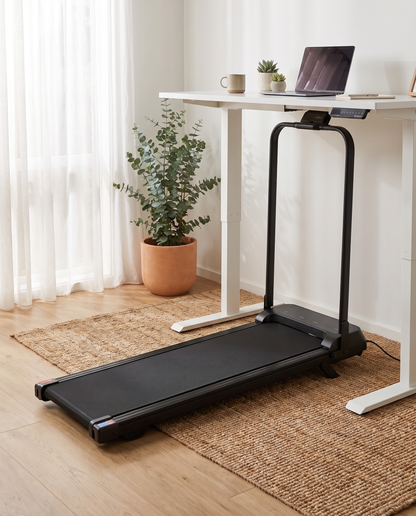 The Aus Walking Pad under a standing desk, handle bar up, side profile